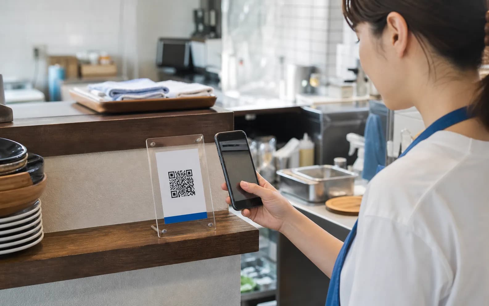 店舗の作業場所に置かれたQRコードをスマホで確認するスタッフ